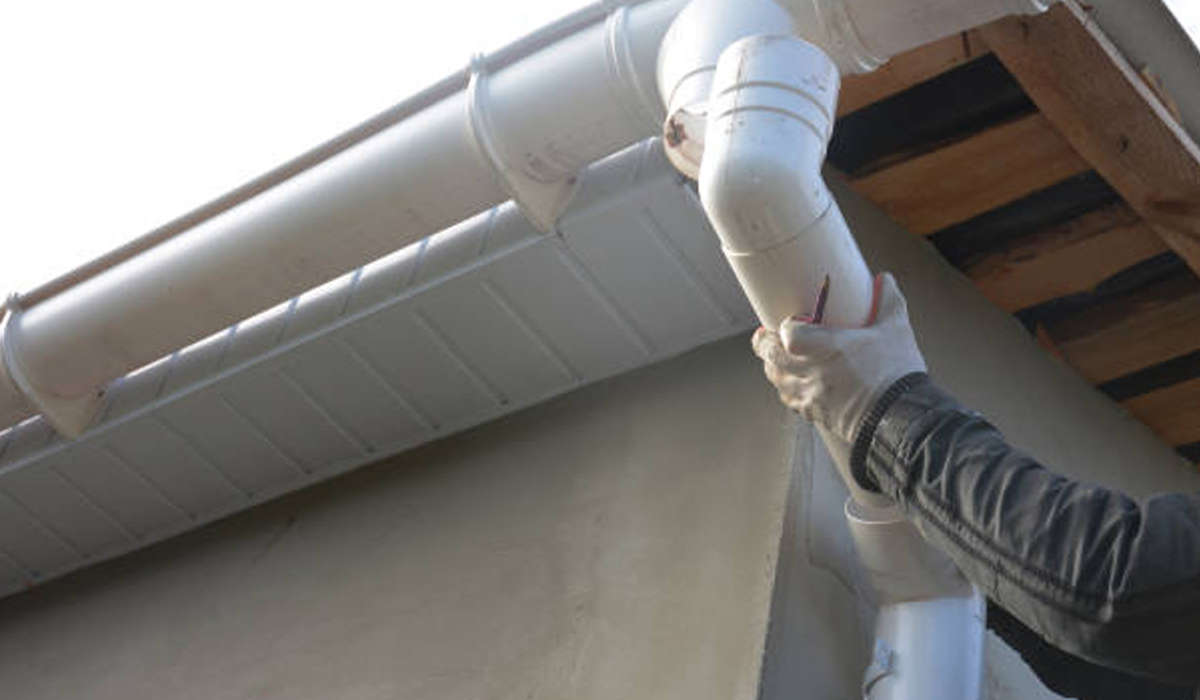 A man fixing the home's downspout. Find experts for replacement on advanced gutters.