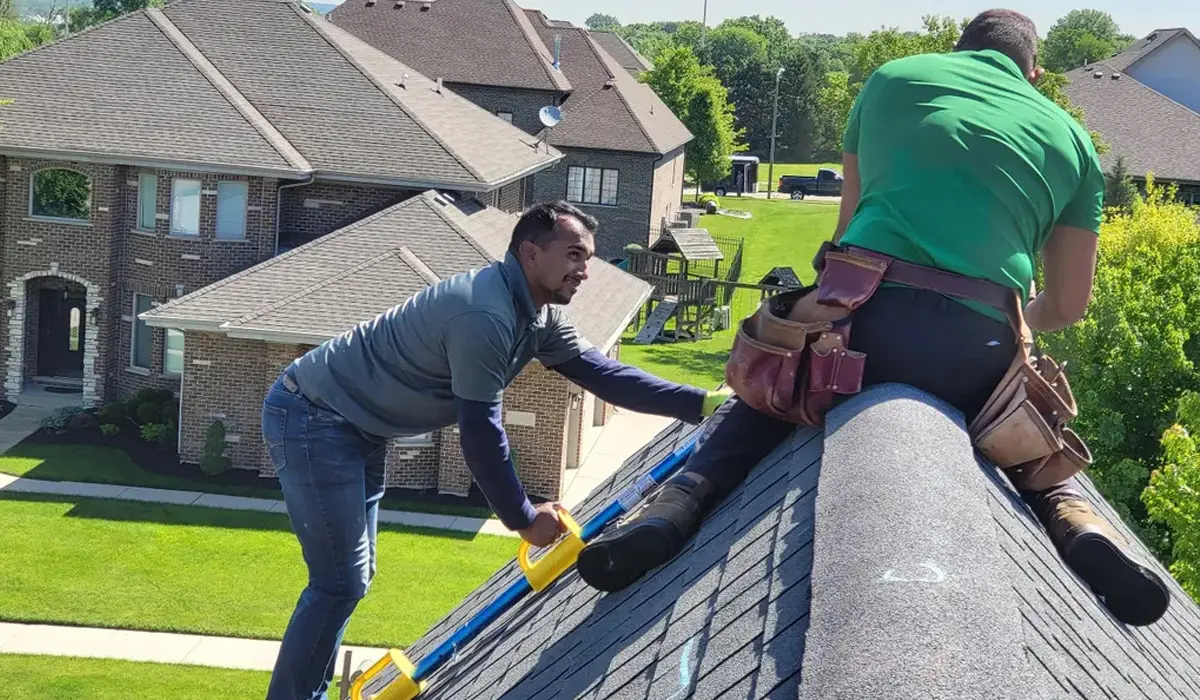 Two men installing IKO roofing shingles on house roof.